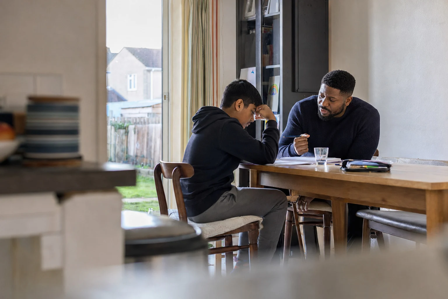 An adult supporting a young person with schoolwork at a table